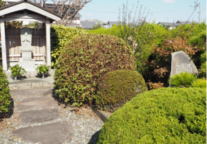 数々の植木と白い駒塚の写真