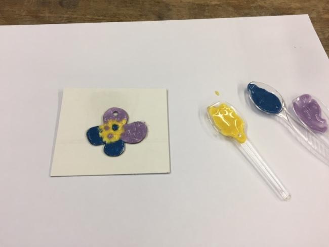 白い紙の上にお花の形に紫・青・黄で色付けしたものと色付けしてあるプラスチックスプーンの写真