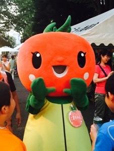 お祭り会場でトマトの顔をした着ぐるみが手を振っている写真
