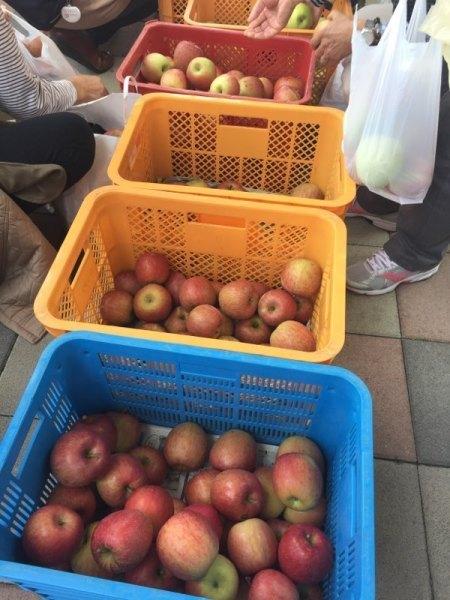 赤、黄色、青のメッシュかごに入った沢山のりんごを買い求める人々の写真