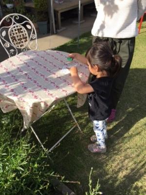 白いイスとテーブルのある庭で女の子が紙を持っている写真