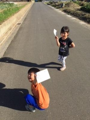 両端に畑のある道路の上で男の子と女の子が紙を持って喜んでいる様子の写真