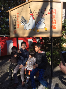 鶏とヒヨコが描かれている開運招福の看板の前で4人の子供が座って写真を撮っている写真
