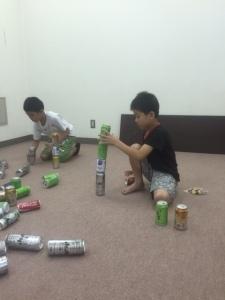 マットの上で男の子2人が空き缶を上に積み重ねている様子の写真
