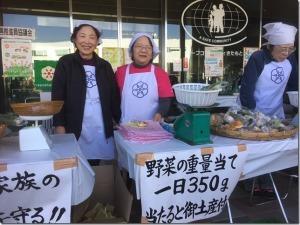 食育ブース内で、野菜の重量当てクイズを担当されている白いエプロンをつけた3人の女性スタッフの写真