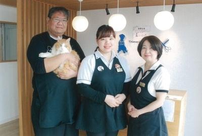 店内で、白と茶色の猫を抱えた男性スタッフとにこやかに微笑む2人の女性スタッフの写真