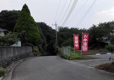 坂道を下る道路の右側に、営業中とお弁当と書かれた2本の赤いのぼりがフェンス沿いに建っている写真
