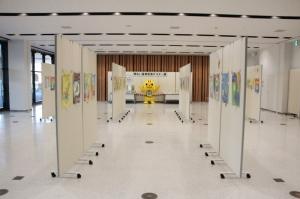 中央にめいすいくんの人形があり、白いボードに作品が張られ展示してある広いロビーの全体写真