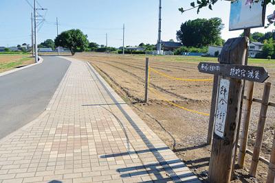 空き地に挟まれた整備された道路と鎌倉街道の道標がある写真