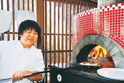 笑顔でピッツァを窯で焼くオーナーシェフの蓮見さんの写真