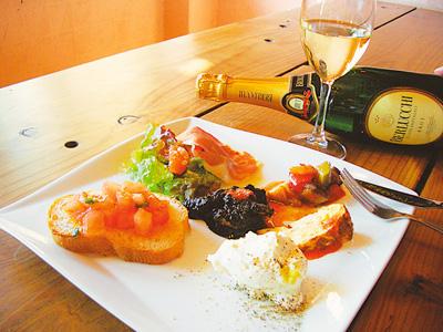 生ハムやパン、サラダなどが乗ったワンプレートのマルサーラの料理とワインの写真