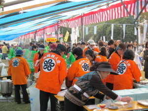 緑の法被を着た人や、オレンジ色の法被を着ている人、来場者で賑わっている様子の写真