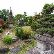 塔やカエルの石像がある、ローズガーデンと和風の庭内の写真