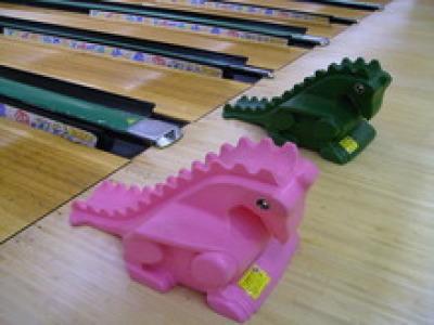 ピンク色と緑の恐竜の形をしたお子様用ボウリング滑り台がレーンの前に2つ並んでいる写真