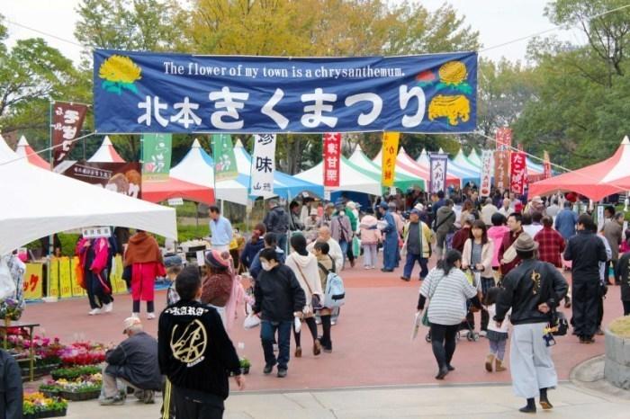 上に北本きくまつりの大きな幕があり多くの出店が並び大勢の人々が集まっている写真