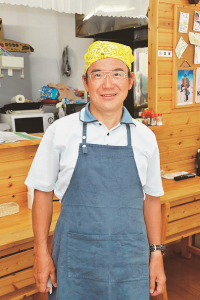 青のエプロンに黄色のバンダナを付けた理事長の上野さんの写真