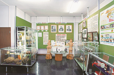 壁には資料がずらりと張られガラスケースには展示物が並べられ埴輪の人形などがある埼玉養蜂資料館内部の写真