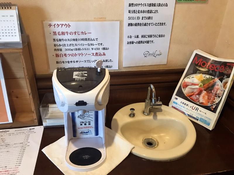 店の入口にある手洗い場に置かれた非接触型のアルコール消毒液噴霧機の写真
