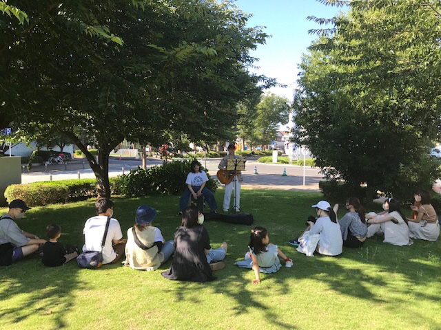 芝生広場でギターを弾く人と木陰に集まって音を楽しむ人たち