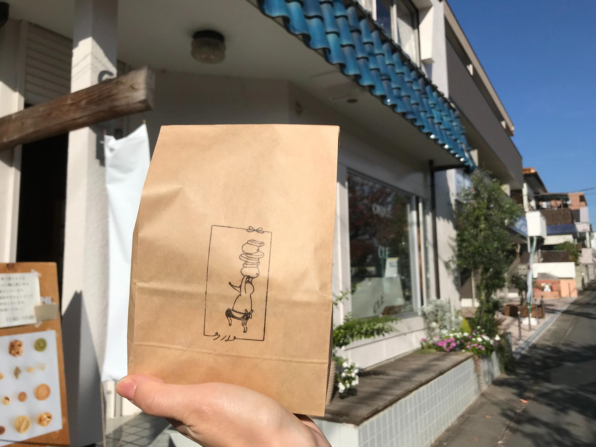 クッキークルの店舗前で、クルのマークの紙袋を手に持っている様子