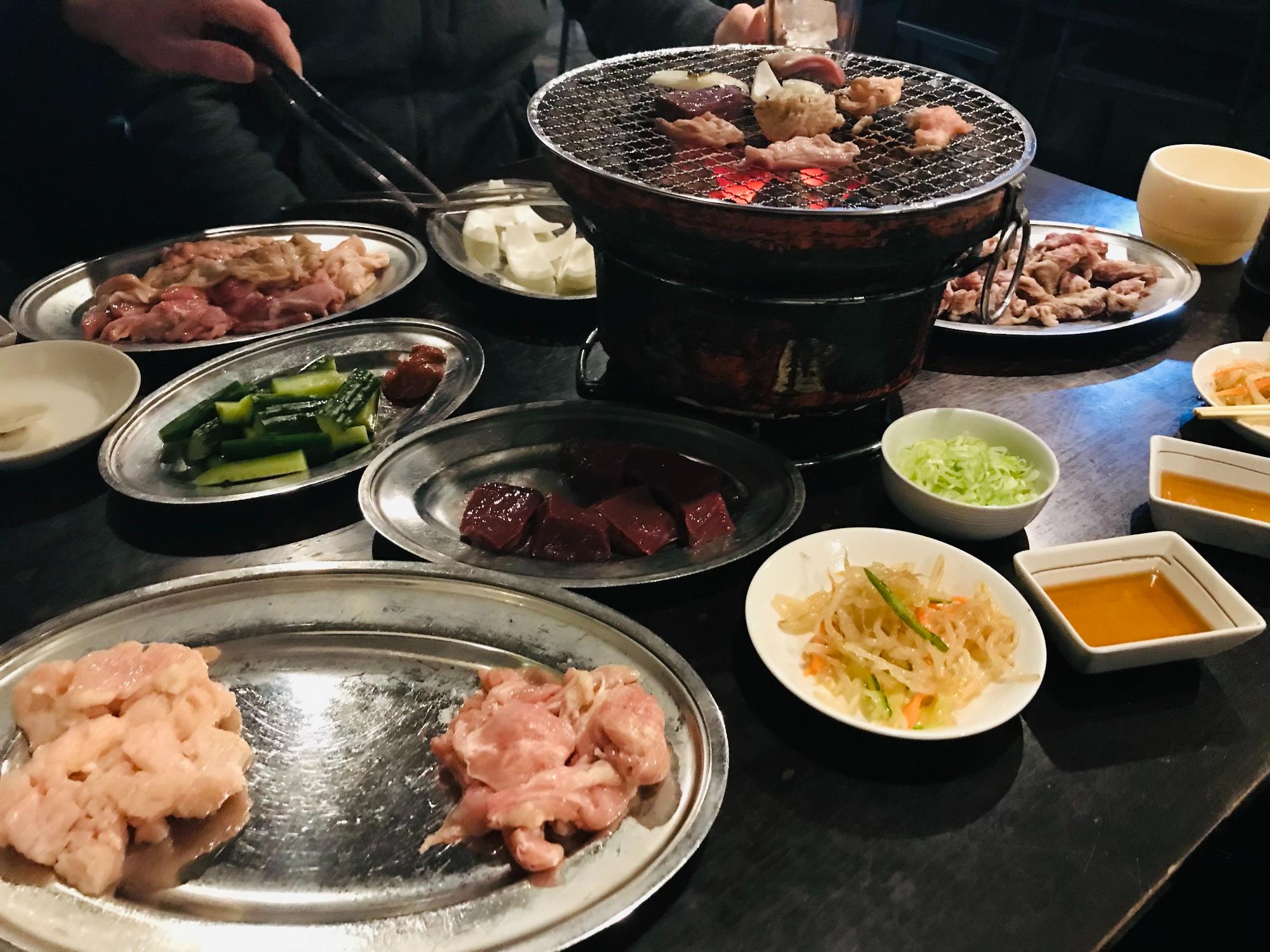 テーブルに並べられた肉と、中央に置かれた七輪で肉を焼いている様子
