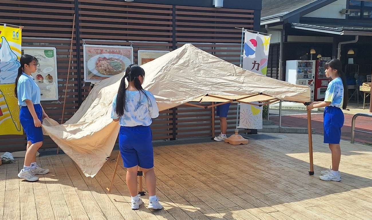 仮設テントの支柱を持つ3人の女の子の写真