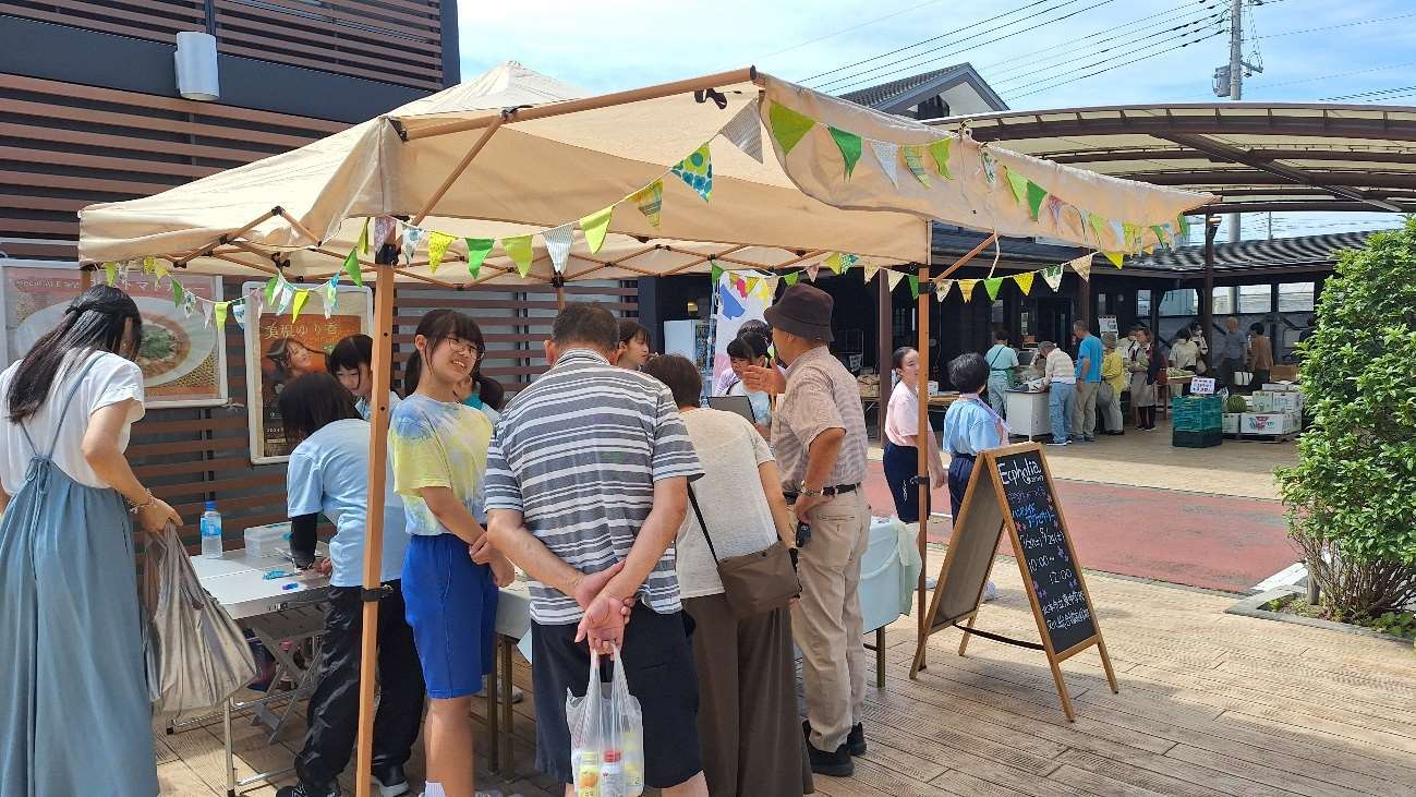 店頭に立つ店頭に立つ部員の皆さんとアクセサリーの置かれた机の上をのぞき込むお客さんの写真
