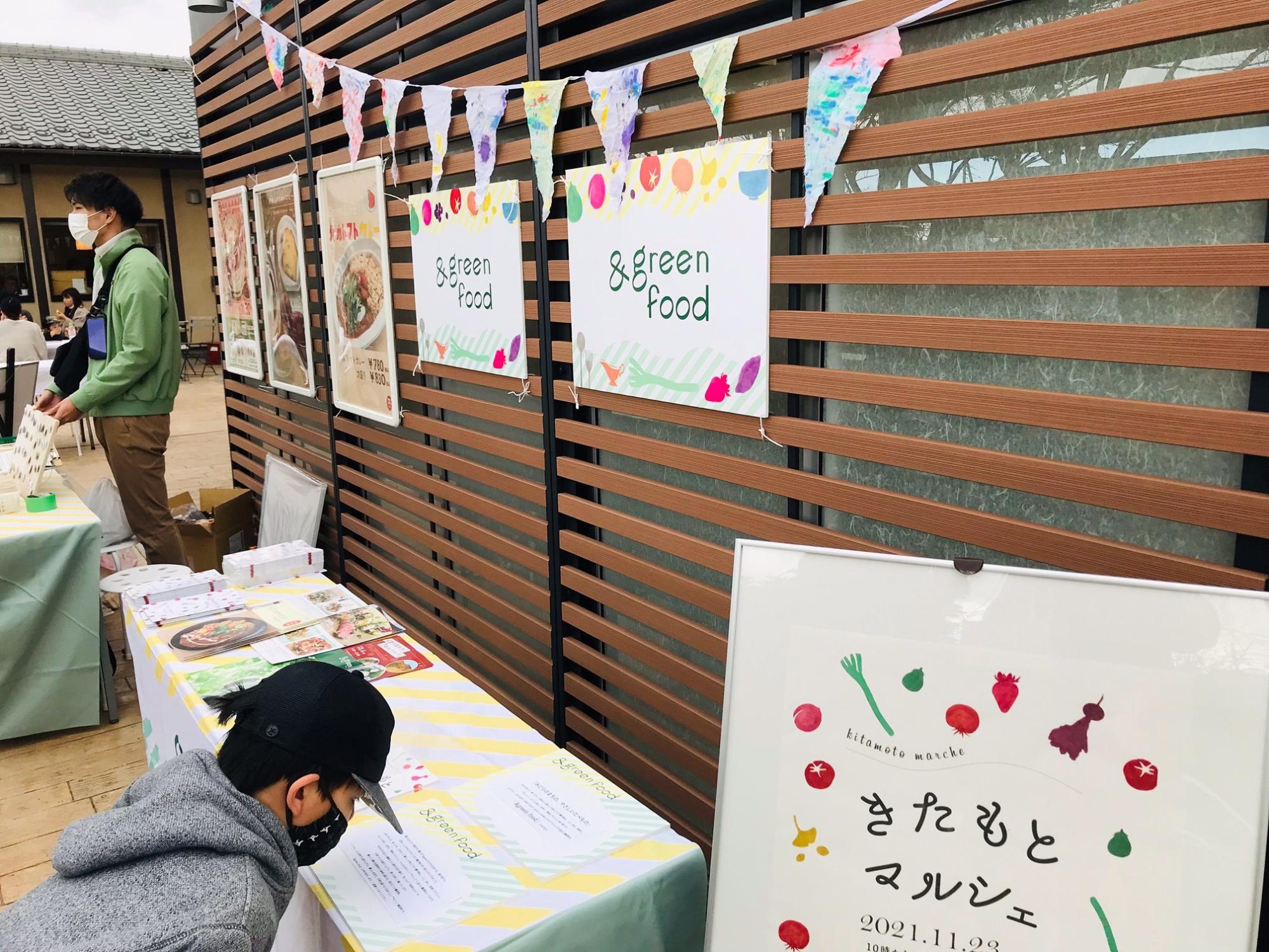 会場入り口に置かれた、きたもとマルシェと書かれた看板と＆greenfoodパンフレットがおかれた机