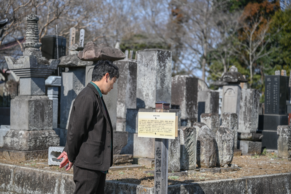 亀御前の供養塔の説明板を読む迫田さんの写真